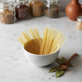 Dry angel hair pasta in a white ceramic bowl on marble surface