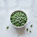 Frozen cut green beans in a white ceramic bowl on marble surface